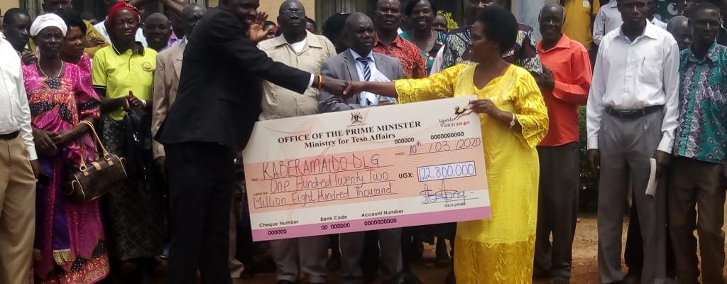 The Minister of State for Teso Affairs Hon. Agnes Akiror Hands over a Dummy Cheque for Micro Projects to the Vice District Chairperson Hon. Oboi Freddrick amidst beneficiaries and the District Technical Staff at the District Headquarters. Dummy Cheque Handover